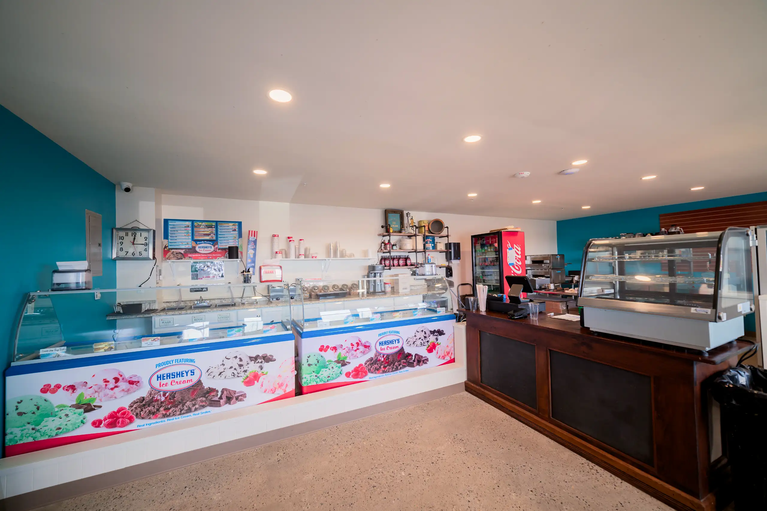 A modern ice cream counter area featuring two large display freezers for Hershey’s ice cream and a dark wood service counter with a glass case.